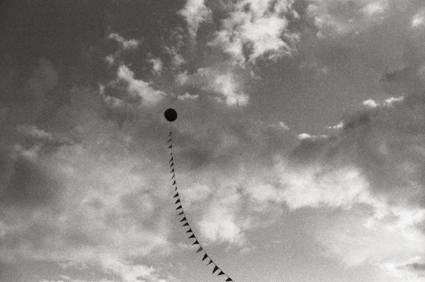 Black and white photo of a cloudy sky with a balloon anchored on a line in the center of the frame. 
