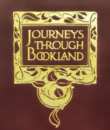 A close-up photo of the decorative gold-stamped titling from a vintage hardcover book bound in red cloth. The words of the title, "JOURNEYS THROUGH BOOKLAND," are arranged in three lines and bordered by a vine and leaf motif in a loosely square-edged rectangle with a fanciful swirl of vines and leaves extending from and centered below the bottom of the border.