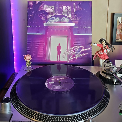 A purple vinyl record sits on a turntable. Behind the turntable, a vinyl album outer sleeve is displayed. The front cover showsa person standing in front of a club that has sign that says "Synth City" . 