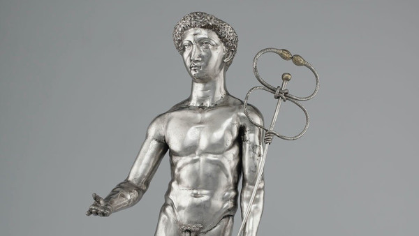 Silver statuette of Mercurius or Mercury, the Roman god associated with Hermes. He has short, curly hair and holds his caduceus in his left hand. His right likely used to hold a money purse. The god is stark naked, not even wearing a cloak.