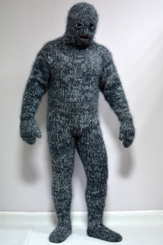 Apparent man in a full knit onesie including gloves, socks, and balaclava head. The knit is dark grey wool and it looks menacing. 
