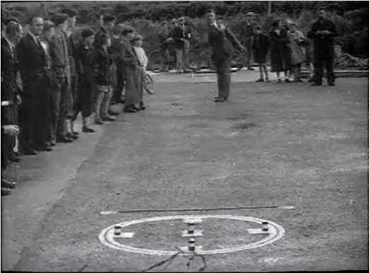 Skittles-style game from black and white archive film. Men throwing carved sticks at a circular target on the ground. 