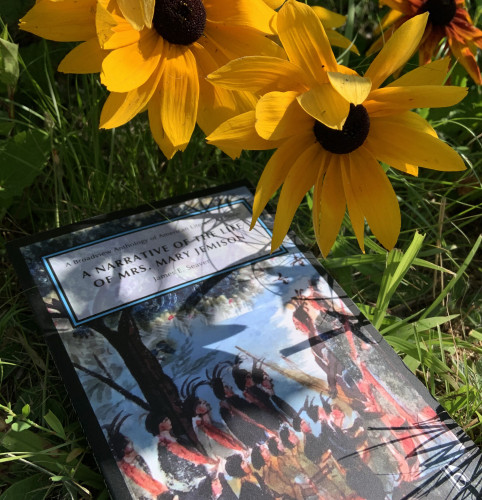 A copy of A Narrative of Mrs. Mary Jemison is lying in the shade on some grass, closely surrounded by orange-yellow flowers.