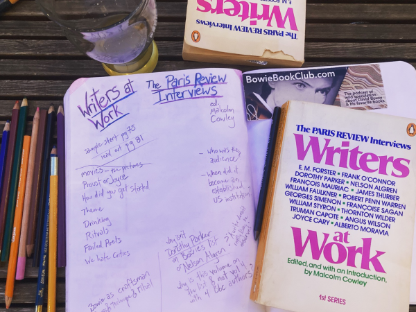 Open notebook with colored pencils and the book Writers at Work: the Paris Review Interviews