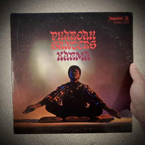 Album cover for Karma by Pharoah Sanders, featuring a photograph of a man in a lotus meditation pose, his arms outstretched 