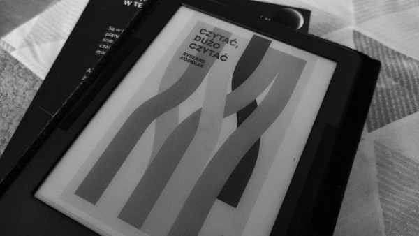 czarno-białe zdjęcie. czytnik ebooków leżący na książce. na czytniku otwarta okładka książki Ryszarda Koziołka... 