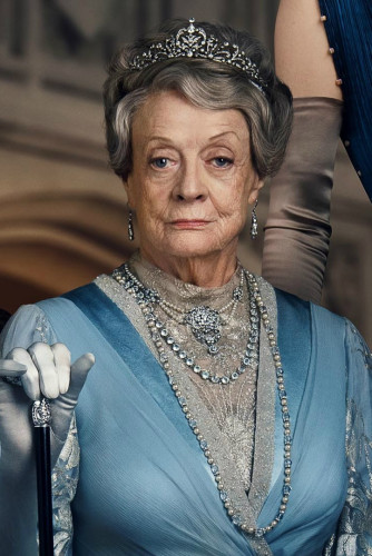Dowager Violet from Downton Abbey (image from the second movie).
She's played by Dame Maggie Smith.
Wearing a satin blue dress, and silver colored jewels with a cane with a silver handle in her hand. She's looking stern but not too unkind.