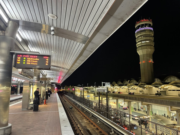 Big art deco air control tower against a night sky. Visible at left is a Metrorail info sign showing trains comin in 2, 3, and 8 minutes