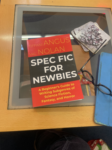 The book ‘Spec-fic For Newbies by Tiffani Angus and Val Nolan on a glass-topped coffee table 