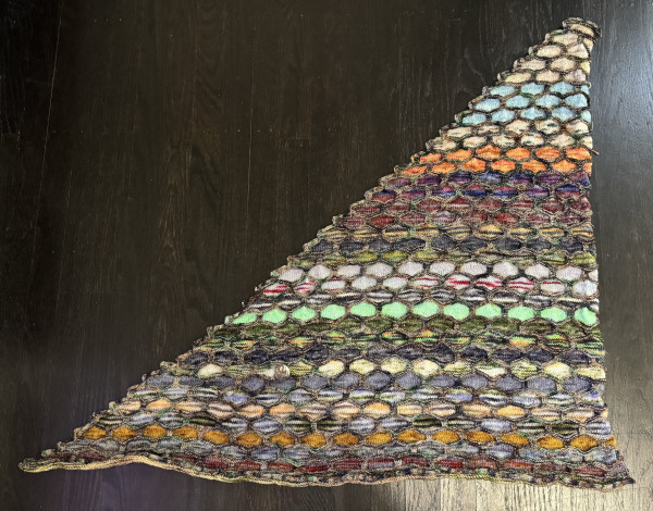 Overview photo of a triangular shawl with a honeycomb pattern. Rows of honeycombs are knit in different colors from a yarn advent calendar