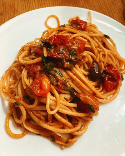 A plate of Spaghetti alla puttanesca which is a very vibrant and fiery looking dish with pieces of olives and tomatoes 