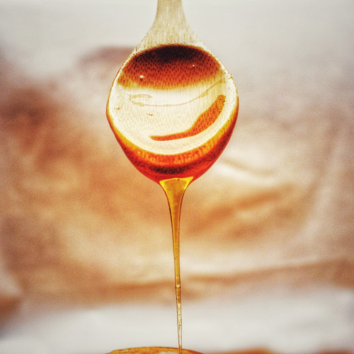 A wooden spoon with honey dripping off of it.