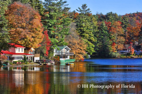 A photograph of a scenic view of Lake Sequoya in Highlands, North Carolina, showing homes that line the shore and autumn colors beginning to turn some of the trees beautiful reds, oranges and browns.