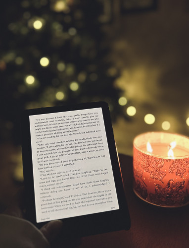 My Kindle, a candle, & a Christmas tree in the background.