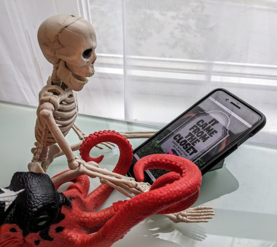 A toy octopus and skeleton reading It Came from the Closet on a phone (that's almost as big as they are)