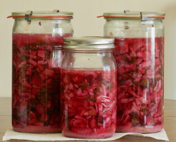 3 canning jars with chopped vegetables immersed in red liquid.