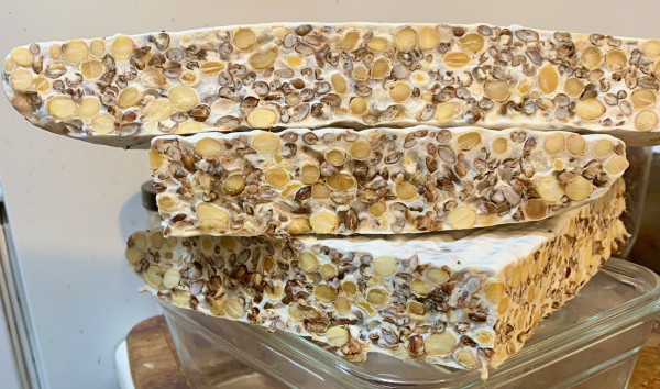 A slab of tempeh sliced so that the cross-section is visible, three pieces stacked.. Large tan ovals from the soybeans, small dark sections from the purple barley, the interstices filled with white mycelium.