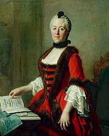 A portrait of Maria Antonia of Bavaria. She looks at the viewer, her hair tightly curled to her head. She wears a low cut gown edged in furs. It is a red gown, and she looks as though the viewer just interrupted her reading.