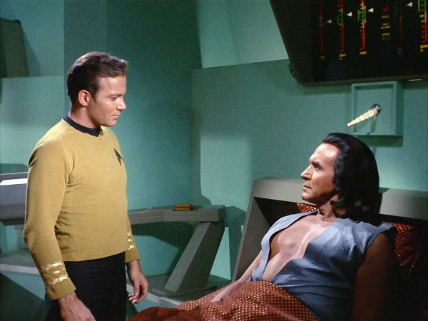 In a scene from "Space Seed," in the original Star Trek series, William Shatner appears as Captain Kirk with Ricardo Montalban as evil mastermind Khan. As Khan reclines on a sickbay bio bed, his tunic is open to the waist. In this frame, Kirk stands over him and appears to be ogling Khan's smooth shaven, well developed, and shapely bare chest, a habit for which Kirk is stereotypically known.