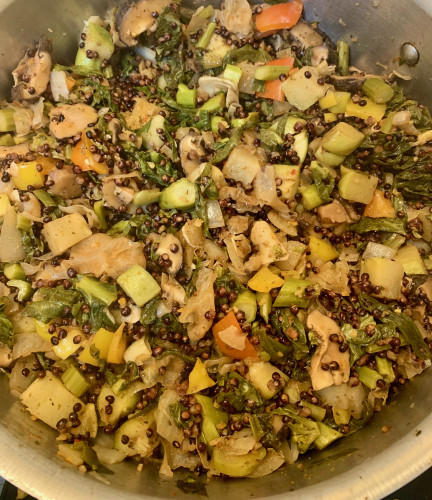 A pot of vegetable stew. Visible are lots of dark grain, green pieces, some leaves, yellow piece, white peces.
