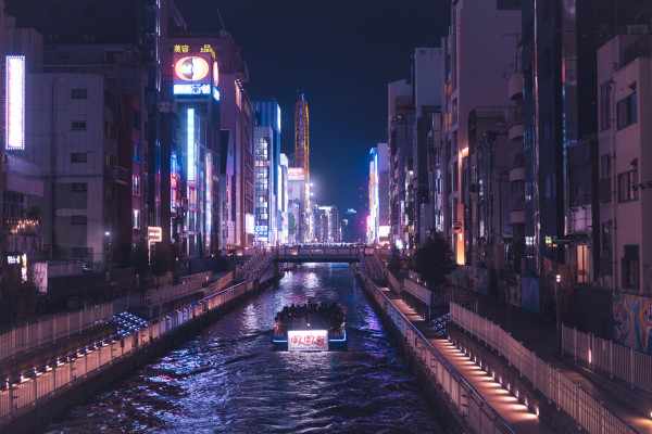 Night shot of a river in the middle of Osaka. A boat takes tourists toward the heart of the city.
