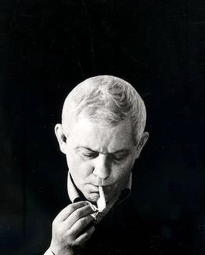 Photographic portrait by AB Bohdziewicz of poet Zbigniew Herbert, in black and white. White-haired Herbert is clad in a black sweater and looking down, lighting a cigarette. 