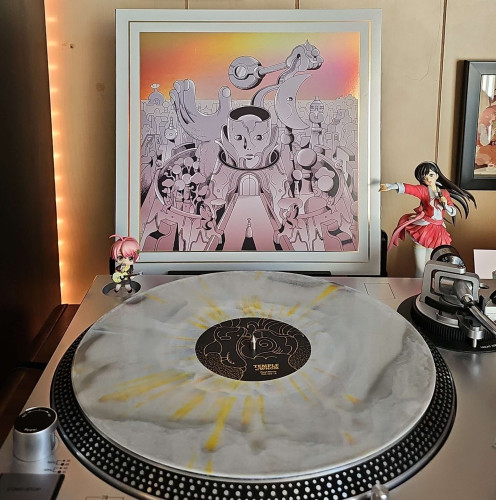 A white and grey marbled w/ yellow splatter vinyl record sits on a turntable. Behind the turntable, a vinyl album outer sleeve is displayed. The front cover shows a futuristic town with a head coming out of the main building, along with an arm and a moon. 