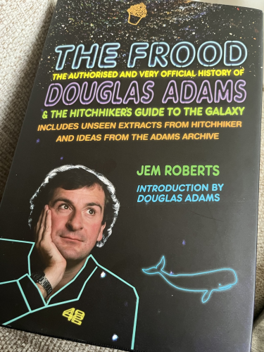 Front cover of The Frood with a photo of Douglas Adams resting his chin on his hand staring out with a background of stars in space and a drawing of a whale and a bowl of petunias falling down.