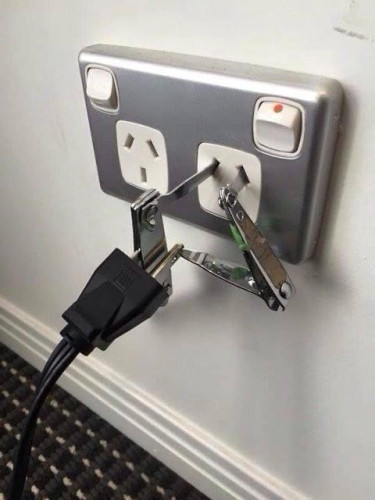 A power plug is connected to a wall socket using nail clippers and a nail file to fashion a makeshift adapter.  The switch is on. 