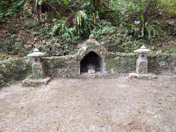 Photograph of the Utūshi for the tomb of Usachiyu. It is located on the side of a paved square, inside the encircling stone wall. It is a small arch made of limestone slabs with an incense burner inside. There are stone lanterns on each side. It clearly is the largest of the three shrines, showing the importance of this Usashiyu lord. 
