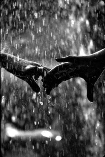 B&W photo of 2 hands touching in the rain.