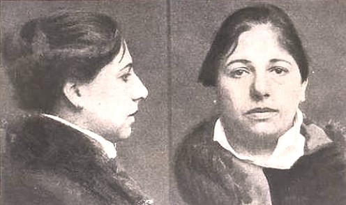 Mug shot of Margaretha Zelle, better known as Mata Hari. There are two angles - one half of the picture is a full profile looking to the viewer's right and the other half is looking straight on at the viewer. She is not smiling and her dark hair is pulled back into a bun. She wears a dark colored warm coat.