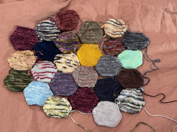25 knitted hexagons (unstuffed) made from scrap fingering yarn.
