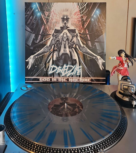 A Silver w/ Blue Splatter vinyl record sits on a turntable. Behind the turntable, a vinyl album outer sleeve is displayed. The front cover shows a metallic android connected to wires. 

To the right of the album cover is an anime figure of Yuki Morikawa singing in to a microphone and holding her arm out. 