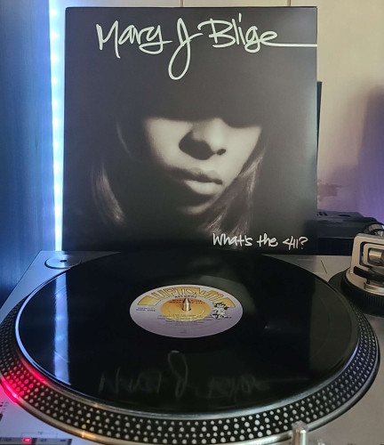Image shows a turntable with a black vinyl record on the platter. Behind the turntable vinyl album outer sleeve is displayed. The front cover shows Mary J Blige's face shot with her eyes and up blocked out by a shadow. 