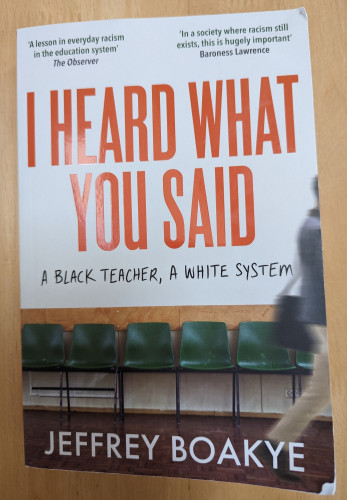 Front cover of the book "I Heard What You Said" by Jeffrey Boakye which shows a row of green plastic chairs with a blurred figure walking out of shot on the right hand side