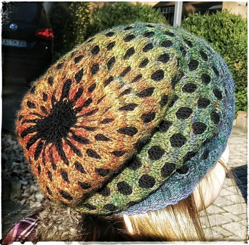 A handknit hat, view from behind the head.

Hat has a basketweave pattern with the overlay in a rainbow colorgradient from blue to green to yellow to orange. The underlaying color is black.