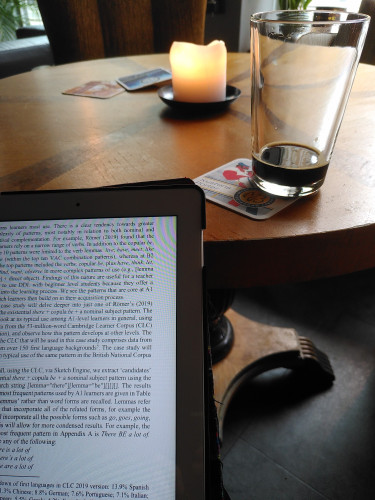 Tablet with academic text on data-driven learning in front, almost empty glass of porter beer in the middle, and a burning candle in the back of the picture.