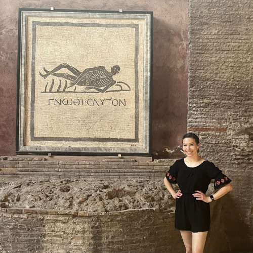Dr G standing next to a black and white mosaic. Description from museum: “The mosaic, from a funerary area, depicts a human skeleton reclined on a symposium couch. He's pointing out at the motto of the Delphic Oracle Gnothi sauton, "know yourself", the advice to know the limits of the human nature and the brevity of earthly life.”
