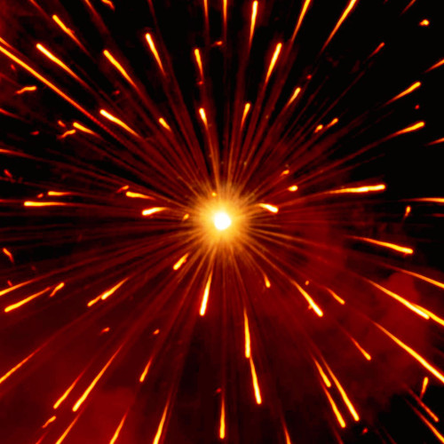 Dark background. A firework explodes in the centre of the picture, creating red clouds, and an array of sparks flying from the centre point, in all directions
