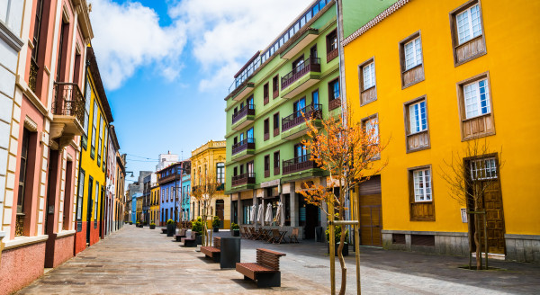 A photo of a street in La Laguna town on Tenerife. There are benches in the middle of the street, flanked by houses in different colours like green, yellow and blue. 