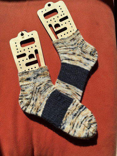 Knitted socks on sock blockers. Pale multi-color main color with dark blue slip stitch arch support on each.