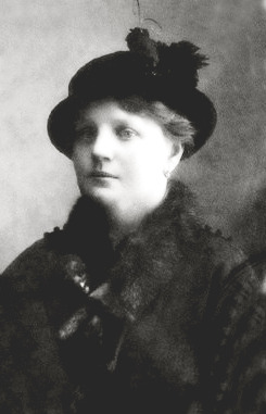 A black and white photograph of Anna Demidova. She looks vaguely to the viewer's left. She wears a very warm looking coat with fur and a decorative hat upon her head.