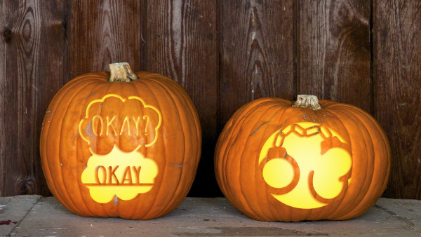 Two pumpkins, one carved with two speech bubbles both expressing consent through the word "OK". The other is carved with handcuffs.