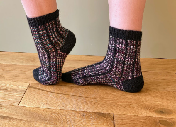 Socks with black and rainbow variegated yarn, with slipped stitches along the whole, having the effect of stained glass columns