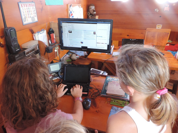 Two girls look at a computer screen that shows Wikipedia content downloaded via Kiwix while on a boat named Kyrimba.