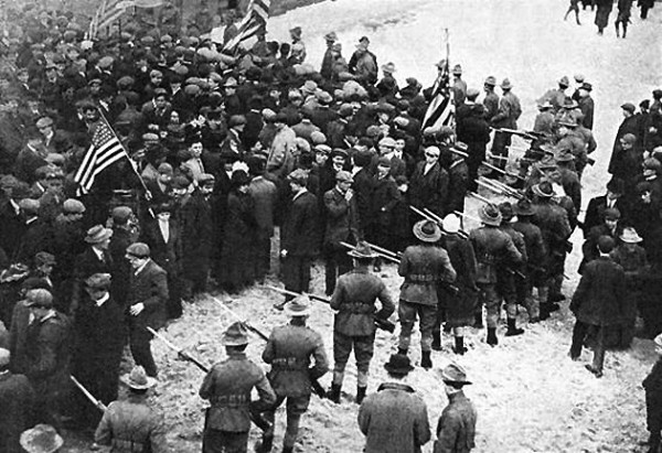 Massachusetts militiamen with fixed bayonets surround a group of strikers, several of whom are carrying American flags on long poles. By http://womhist.binghamton.edu/teacher/DBQlaw2.htm, Public Domain, https://commons.wikimedia.org/w/index.php?curid=131378