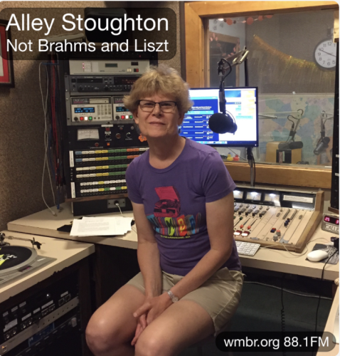 Photo of Alley Stoughton sitting on a stool in “B Control” of WMBR, with the control board behind her.