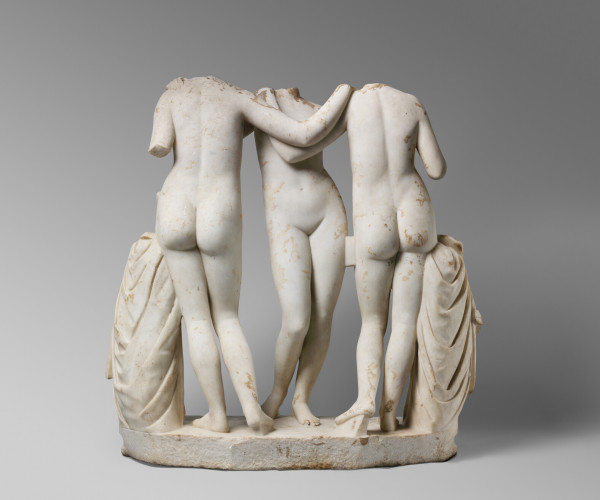 Three women stand nude with two facing away from the viewer and one facing towards the viewer. They are missing their necks and heads.