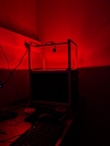Dark room with a dark box. There is red light coming out of the top of the box, dimly illuminating the picture.